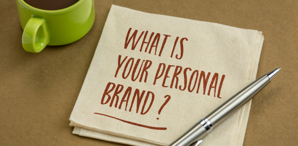 Beige napkin with the handwritten message What is your personal brand next to a green coffee mug and a silver pen