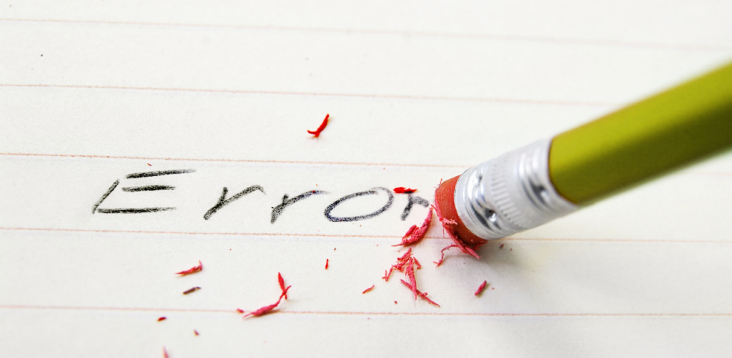 Sharpened green pencil erasing the word Error from lined paper, leaving pink eraser shavings scattered on the page