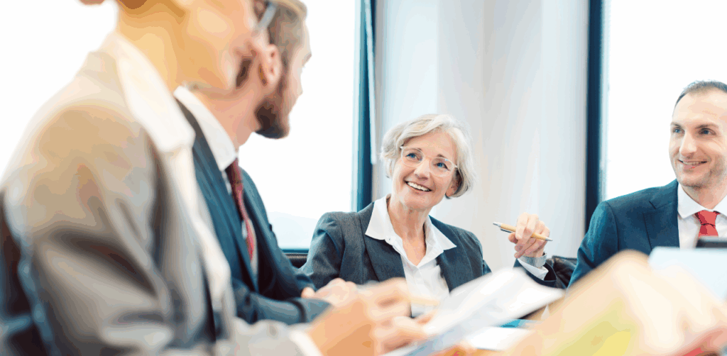 A group of professionals in suits smile and converse during a meeting in a bright, modern office