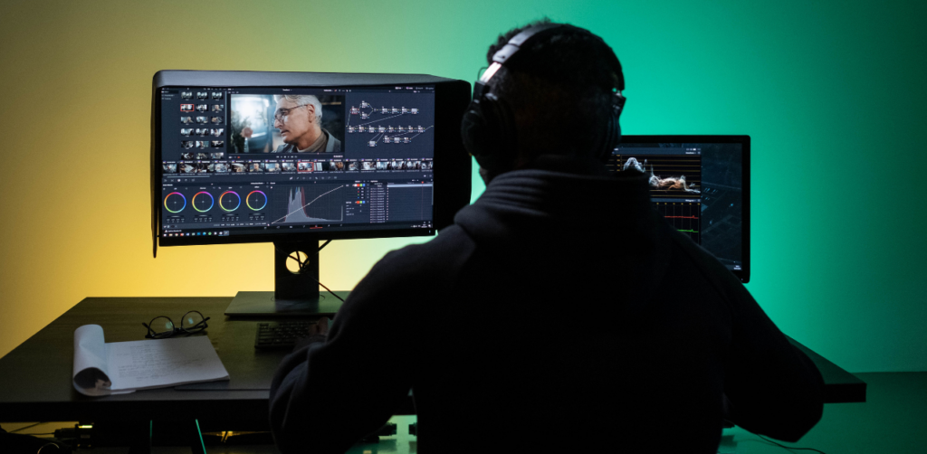 Video editor wearing headphones works on color grading at a dual-monitor setup