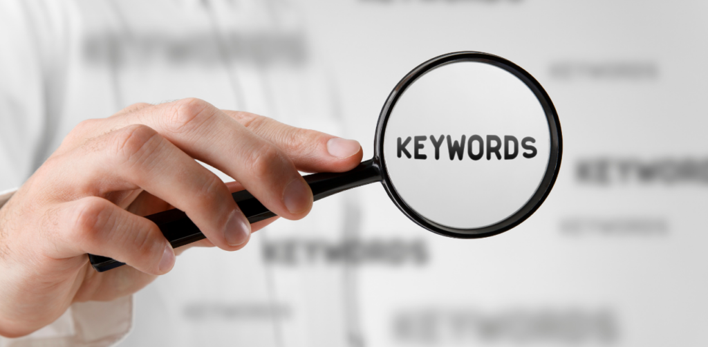 Hand holding magnifying glass focused on the word “keywords,” highlighting keyword research