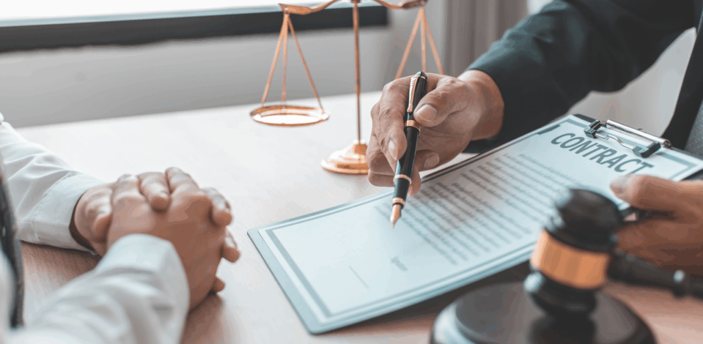 Lawyer pointing at contract while client listens, with gavel and scales of justice on table