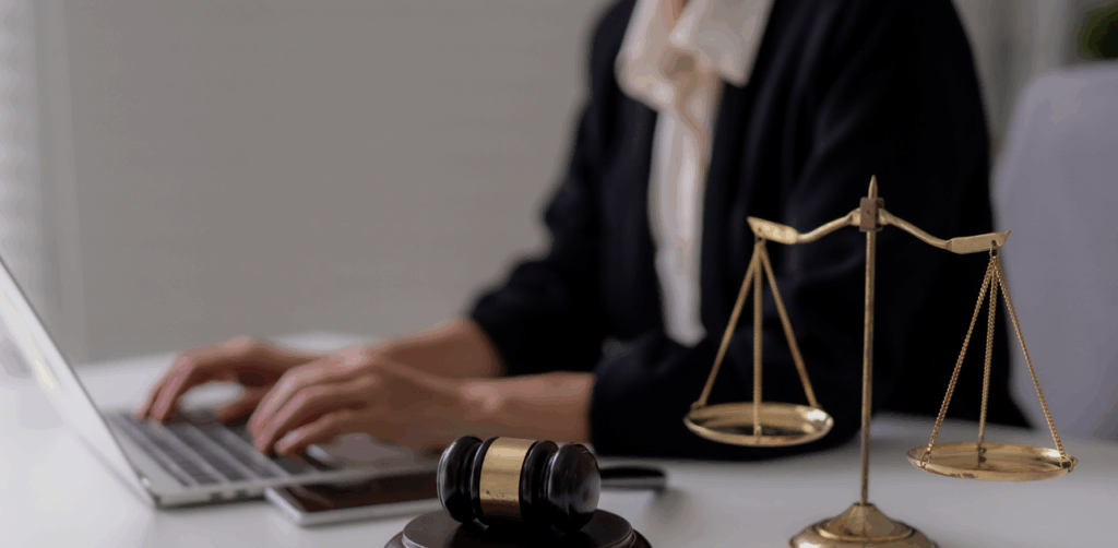 Lawyer typing on laptop with justice scales and gavel on desk in office