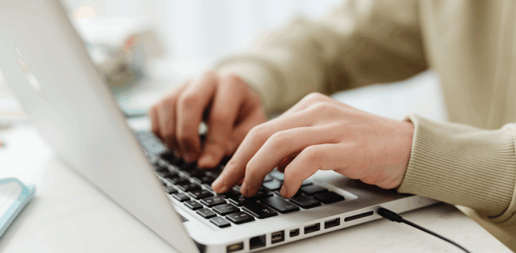 Person typing on a laptop keyboard at a white desk, focused on digital tasks