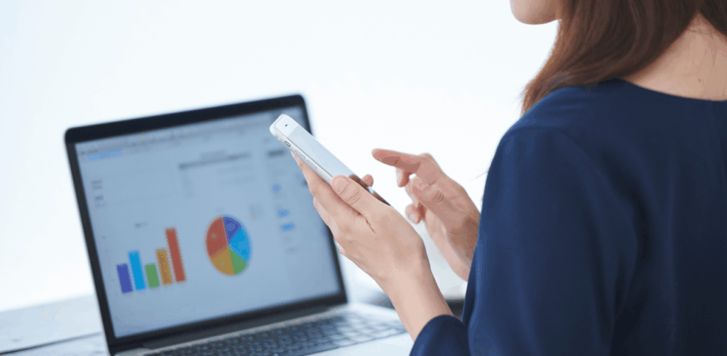 Woman using smartphone while analyzing colorful data charts on a laptop
