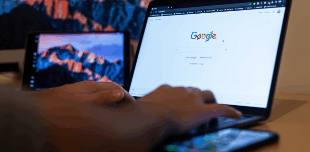 Person typing on a laptop with Google search open, phone and tablet in view