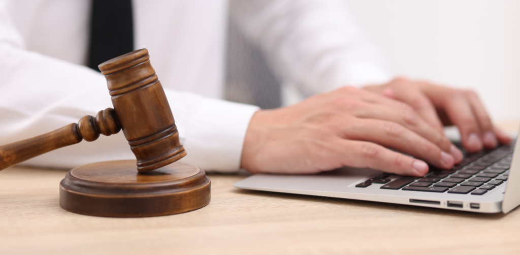 Close-up of a gavel beside a person typing on a laptop, symbolizing legal work, law practice, and digital documentation