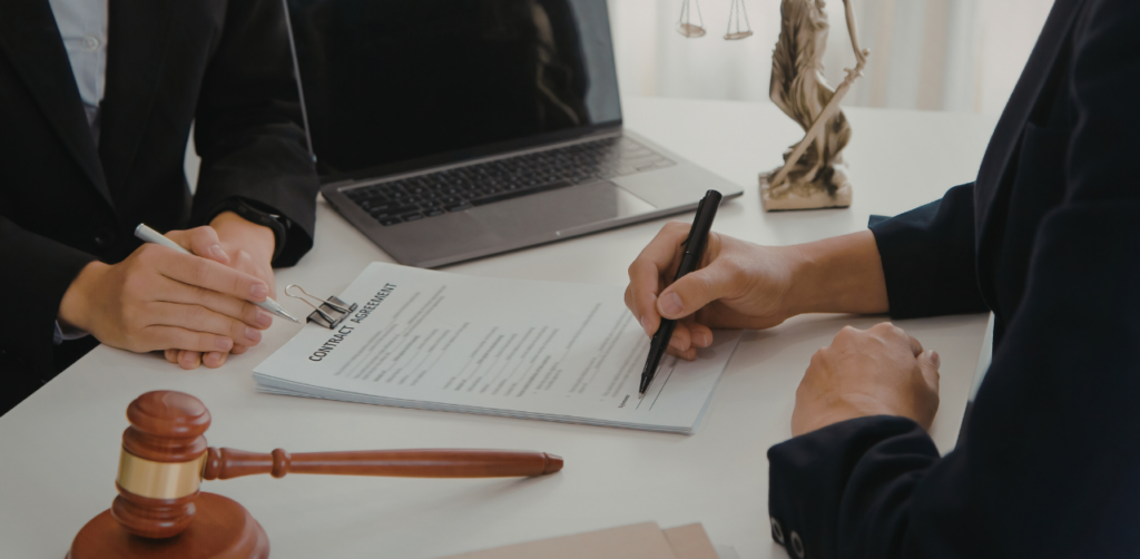 Client signing a contract agreement with a lawyer at an office desk, with legal documents and gavel nearby